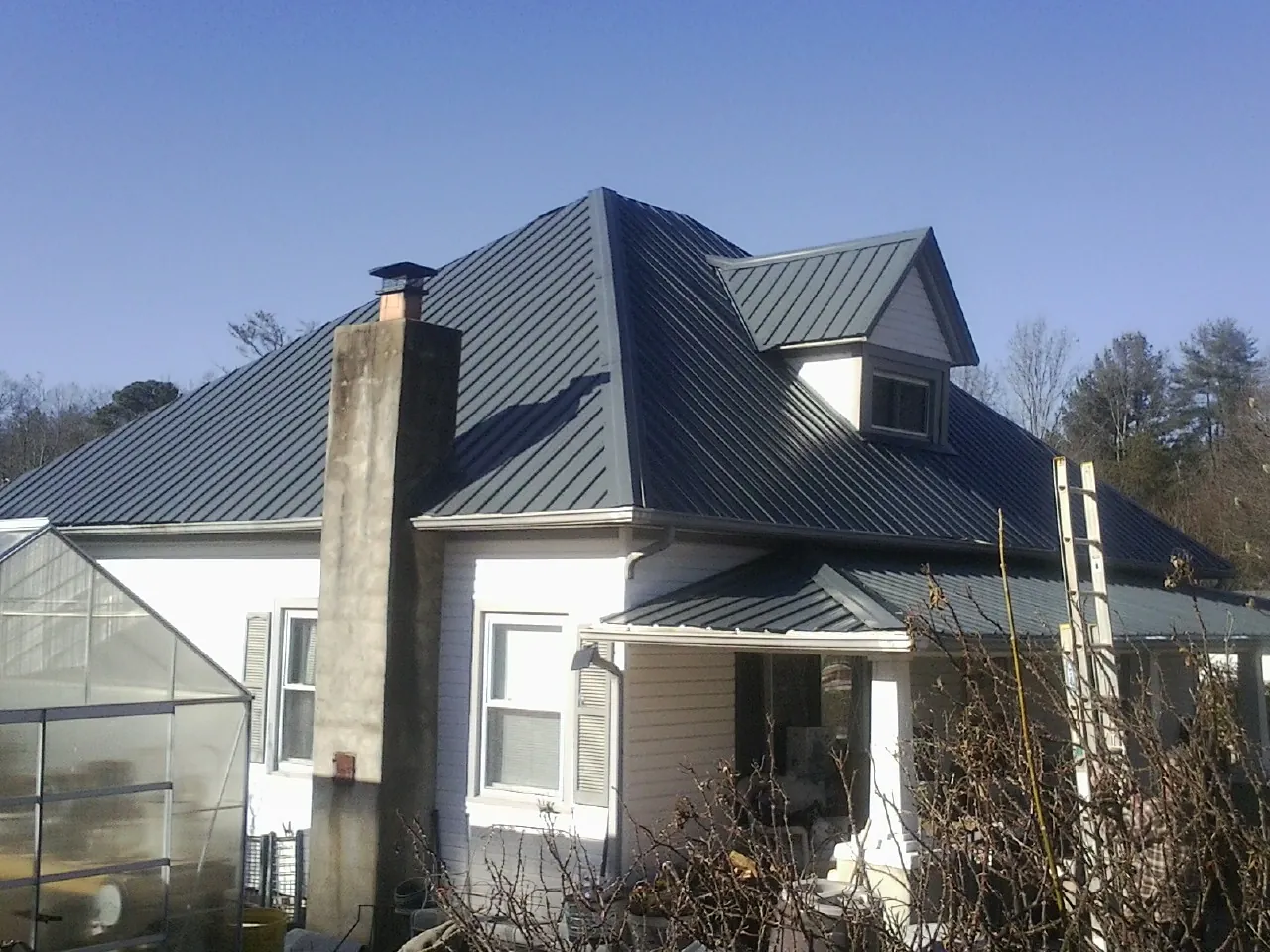 Dark blue standing seam metal roof on a white farmhouse with dormer — Slate & Tile Roof Repair by Roofing Brothers in Hooker