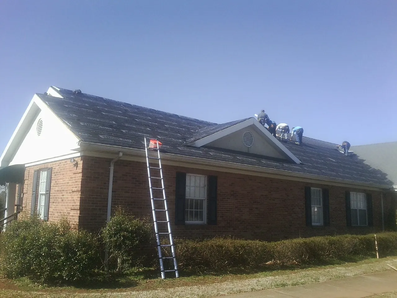 Crew tearing shingles off a brick ranch roof with a ladder set — Metal Roof Repair work by our crew in Hooker