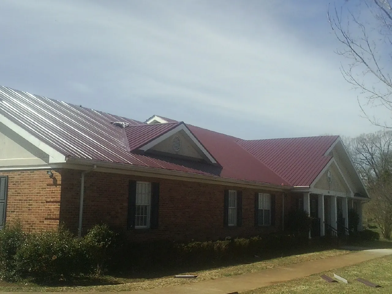 Red metal roof with gabled entries on a long brick building, from a Hail Damage Roof Repair job in Hooker