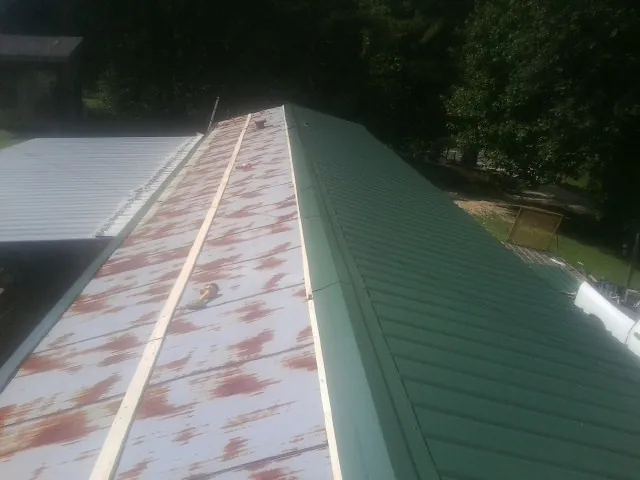 Old rusted panels beside newly installed green metal roofing — Wind Damage Roof Repair by Roofing Brothers in Hooker
