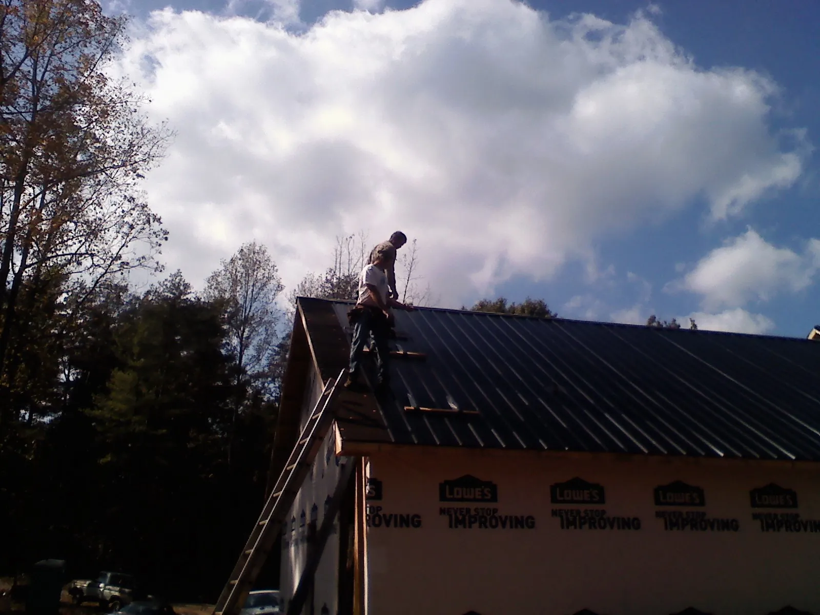 Roofer fastening dark metal panels high against a cloudy sky, from a Roof Inspection job in Hooker