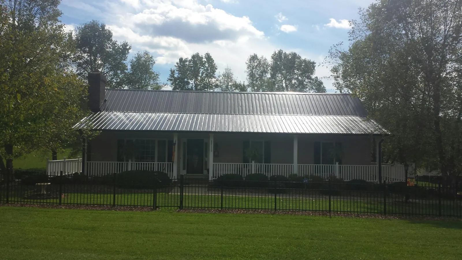 Gray metal roof on a brick ranch with a full width front porch — Gutter Guard Installation work by our crew in Hooker