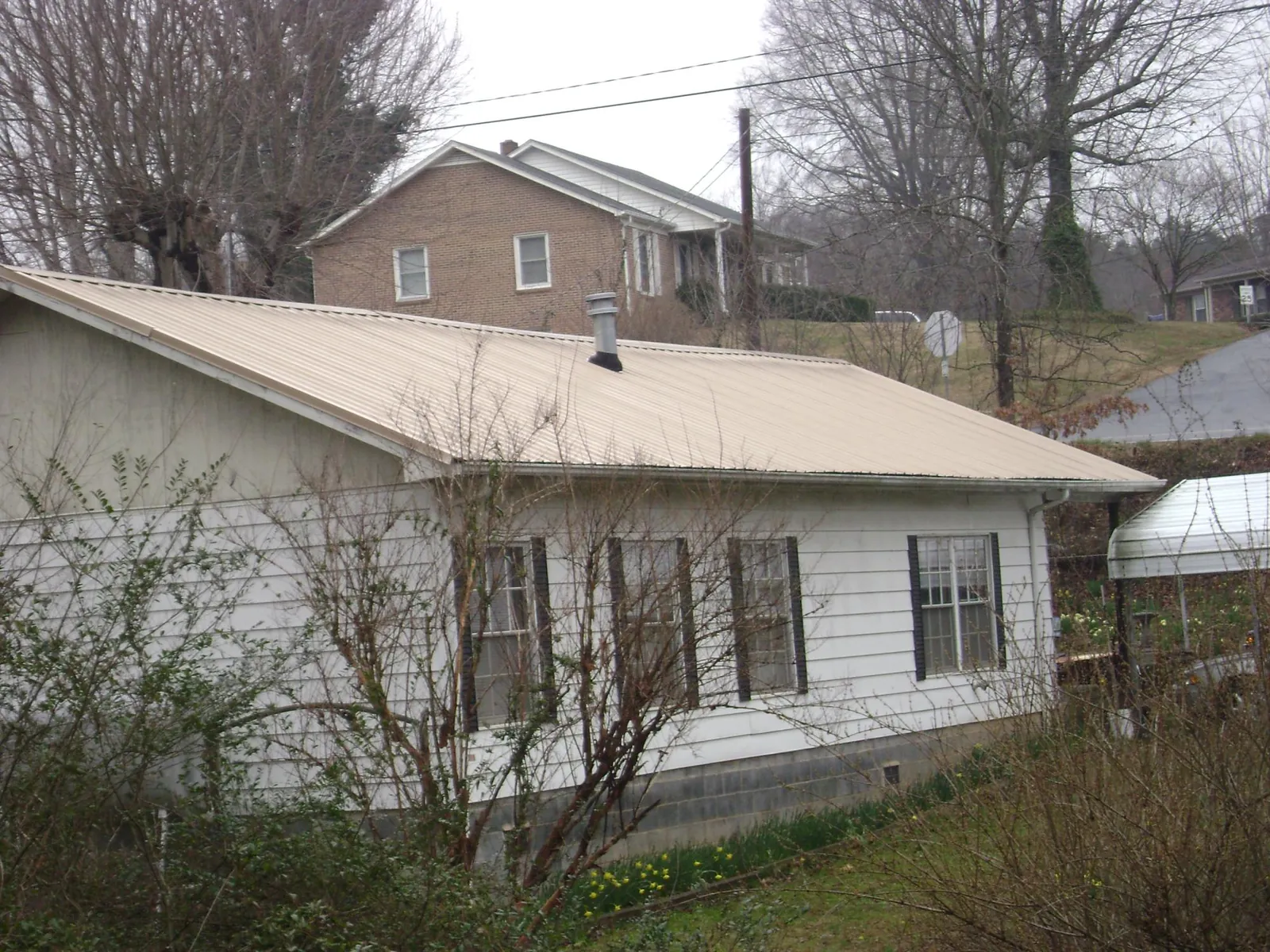 Tan metal roof on a white sided house set into a hillside — Commercial Roofing by Roofing Brothers in Hooker