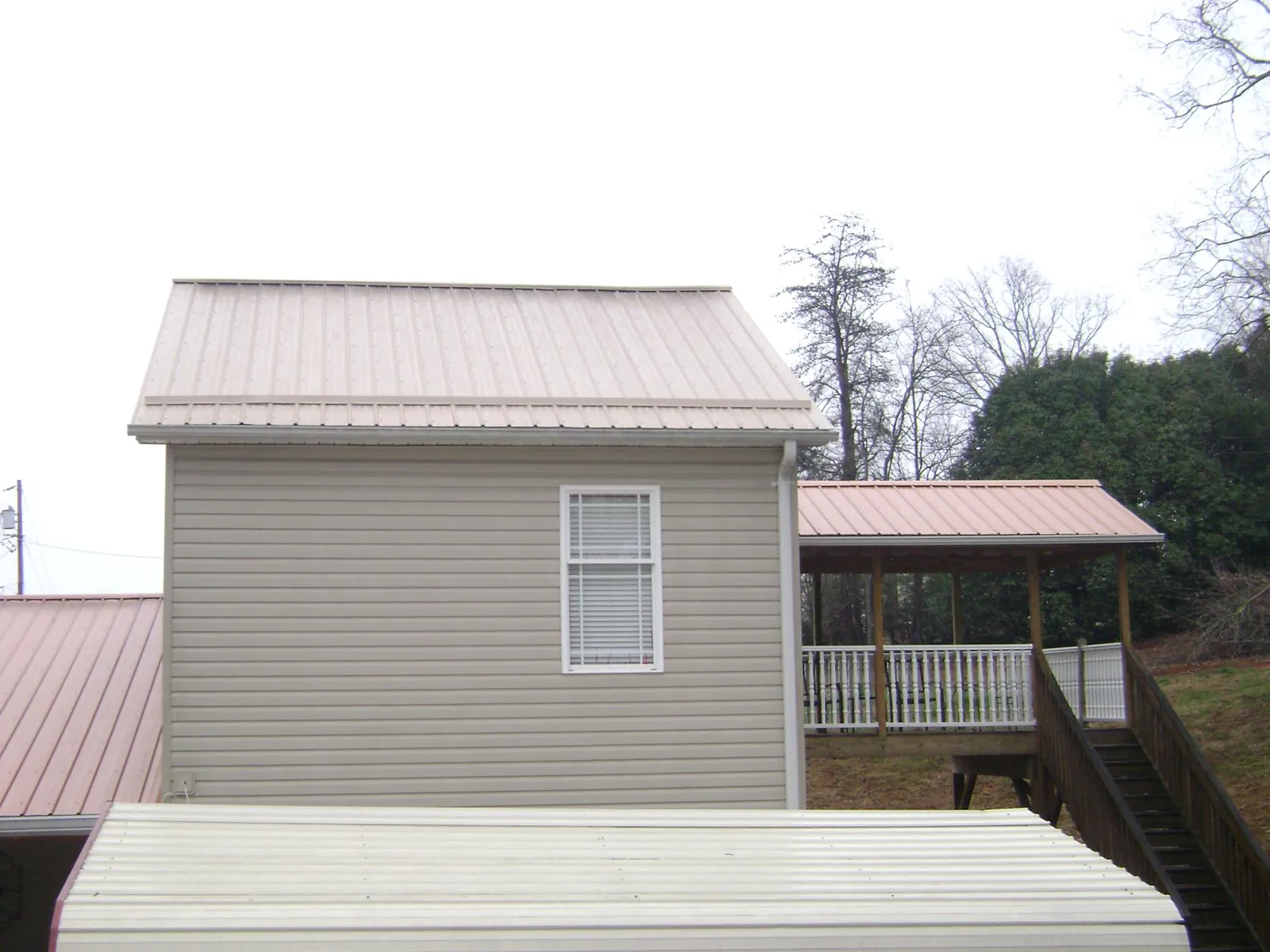 Tan metal roofs on a two story addition and attached porch, from a Roof Replacement job in Hooker